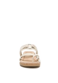 Beige slide sandals feature a knotted fabric strap, a circular metallic accent, and a textured cork footbed for comfort.