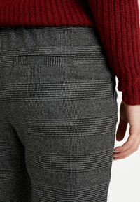 Svart- och vitrutiga byxor i texturerat tyg, med en bakficka och elastisk midja, kombinerade med en stickad vinröd tröja.