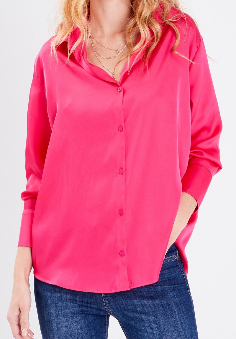 Chemise bouton-up en satin rose avec une coupe décontractée, des manches longues et un col pointu, présentant une texture lisse et un léger brillant.