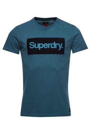 Blaues T-Shirt mit kurzen Ärmeln und Rundhalsausschnitt mit einem schwarzen rechteckigen Aufnäher und türkisfarbenem "Superdry."-Schriftzug zentriert auf der Brust.