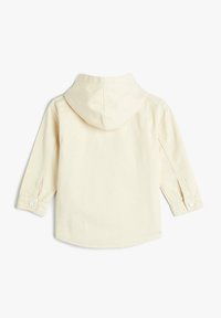 Lys beige hættebluse med lange ærmer, trykknapmanchetter og lige kant. Fremstillet af et blødt, bomuldsrigt stof med en glat tekstur.