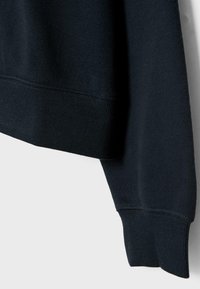 Felpa blu navy con polsini e orlo a costine. Texture morbida con una vestibilità standard, evidenziando i dettagli delle cuciture lungo le giunture.