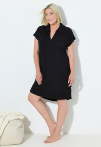 Vestido negro de manga corta hecho de una tela suave, con un cierre frontal de botones y un bolsillo en el pecho. Tiene un corte relajado y un dobladillo a la altura de la rodilla.
