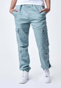 Lichtblauwe cargobroek met elastische boorden, voorzien van meerdere zijzakken, een relaxte pasvorm en soepele katoenen stof. Gepaard met witte sneakers.