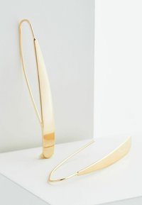 Guldtonede forlængede øreringe med et glat, buet design, der har en minimalistisk form og subtil glans.