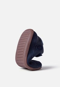 Scarpa in suede morbido di colore blu scuro con suola in gomma marrone, caratterizzata da una forma arrotondata e chiusura con velcro. Presenta dettagli testurizzati.