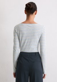 Gestreept top met lange mouwen in lichtblauw en crème, met een brede halslijn en een crop lengte, gecombineerd met donkergekleurde broek met hoge taille.