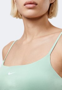 Κοντινό πλάνο γυναίκας που φοράει φωτεινό πράσινο φανελάκι Nike με λεπτές λωρίδες, εμφανίζοντας τον λαιμό, τους ώμους και τα χείλη της.