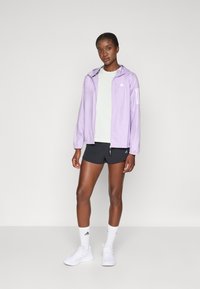 Light purple zip-up jacket with hood, elastic cuffs, three white stripes on the left sleeve, worn over a light green top and black shorts.