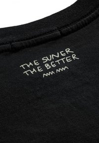 Black cotton shirt collar with white text "THE SUNER THE BETTER" embroidered near the neck, featuring a smooth, even texture.