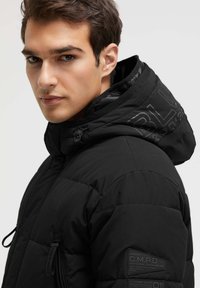 Schwarze Daunenjacke mit hohem Kragen und Kapuze. Verfügt über eine Reißverschlusstasche, strukturierter Stoff und Logo-Details an Ärmel und Kapuze.