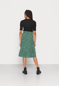 Top negro de manga corta acanalado combinado con una falda midi de estampado floral verde. La modelo lleva botas negras hasta el tobillo. Diseño simple, corte hasta la rodilla.