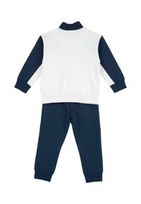 Ensemble de survêtement deux pièces en bleu marine et blanc. Le haut comporte un col montant, un devant blanc et des manches bleu marine ; le pantalon est entièrement bleu marine avec des ourlets resserrés.