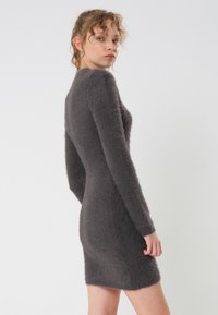 Enganliegender dunkelgrauer Kleid aus weichem, flauschigem Material mit langen Ärmeln und rundem Ausschnitt, knielang geschnitten.