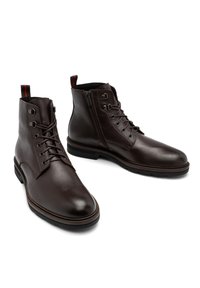 Brązowe skórzane botki za kostkę z okrągłymi noskami, sznurowaniem i zapięciem na zamek, delikatną teksturowaną powierzchnią oraz kontrastującą czerwoną pętelką.