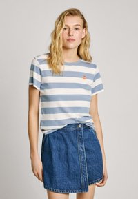 T-shirt à manches courtes rayé en bleu clair et blanc, arborant un petit logo orange, associé à une jupe trapèze en denim.