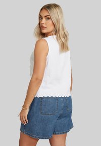 Top blanco sin mangas con tejido texturizado y dobladillo en forma de concha, combinado con pantalones cortos de denim azul que cuentan con bolsillos de parche y un corte relajado.