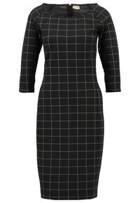 Mustakulum pitkähihaisti mekko, jossa on valkoinen ruutukuosi. Suunnittelussa on pyöreä kaula-aukko ja vartalonmyötäinen leikkaus.