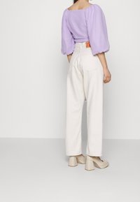 Lila puffärm top tillsammans med vita, högmidjade vida byxor. Notabla detaljer: rektangulär halsringning, texturerad tyg och beige klackskor med blockhäl.