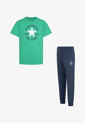 Maglietta in cotone verde con stampa nera e grafica a stella, abbinata a pantaloni jogger blu navy con un piccolo logo sulla coscia sinistra.