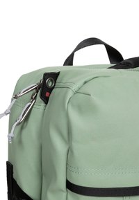 Zaino in tessuto verde caratterizzato da una forma strutturata, dettagli neri, spallacci regolabili e accessori in metallo per attacchi.