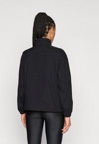 Μαύρο μπουφάν με μακριά μανίκια, ψηλό γιακά και ελαστικά μανσέτες. Διαθέτει άνετη εφαρμογή και λιτό σχεδιασμό· κατασκευασμένο από λείο ύφασμα.