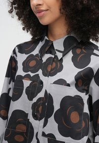 Close-up of person wearing gray button-up shirt with large black and brown floral patterns and two front chest pockets.