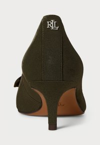 Grønn semsket høyhælte sko med en buet bakdel, som har en sølvlogo og et strømlinjeformet design. Hælen er tynn og spiss.