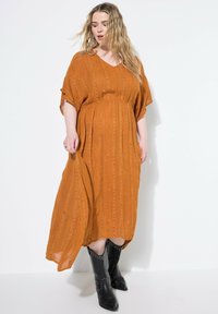 Krustfarbendes, knielanges Kleid mit V-Ausschnitt, kurzen Ärmeln und strukturierter Stoffqualität, die vertikale Streifen und dezente Verzierungen aufweist.