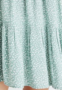 Light green dress with white leaf patterns, featuring a gathered tiered bottom and soft fabric texture.