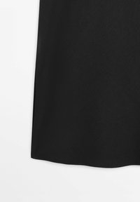 Nahaufnahme eines schwarzen Stoffs, der den unteren Saum und den Seitenschlitz eines Rocks vor weißem Hintergrund zeigt.