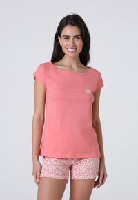 T-shirt rosa corallo a maniche corte con scollo a giro, abbinato a pantaloni corti a stampa floreale in rosa chiaro e bianco. Presenta un piccolo logo come accento.