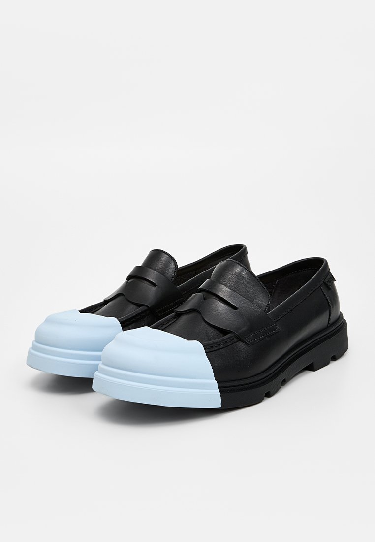 Scarpe slip-on in pelle nera con una punta in gomma blu chiaro, caratterizzate da due cinturini decorativi sulla parte superiore del piede e una suola nera spessa.
