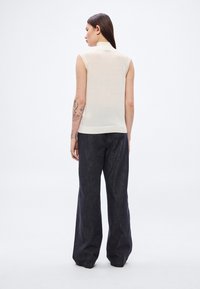 Ujjatlan krémszínű felső magas nyakkal, sötét, bő szárú nadrággal párosítva. A felső puha, könnyű anyagból készült, testhez simuló szabással.