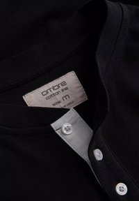 Černá bavlněná košile se šedým límcem, se dvěma bílými knoflíky a štítkem se nápisem "ombre bavlněná řada, velikost M."