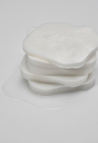 Pile de coussinets de coton blancs et mouillés avec du liquide absorbé visible sur une surface lisse et gris clair.