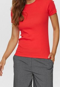 T-shirt rouge ajusté à manches courtes en tissu lisse, associé à un pantalon large à rayures grises avec poches latérales.