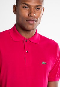 Rode poloshirt, kraag met twee knopen, gestructureerde stof, met een klein groen krokodillenlogo op de linkerborst.