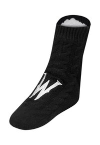 Calzini pantofole neri lavorati a maglia con motivo a treccia, con una "W" bianca sulla parte superiore e morbido rivestimento interno in pile bianco.