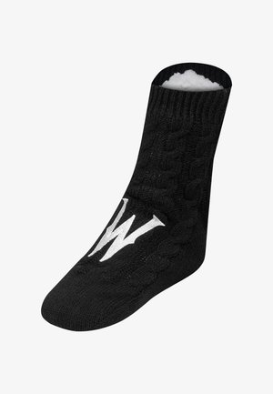 Chausson en tricot noir avec un motif en câble, "W" blanc sur le dessus, et doublure en polaire blanche douce à l'intérieur.