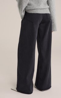 Jeans negros de pierna ancha hechos de denim, con un diseño clásico de cinco bolsillos y detalles de costura sutiles. Llevados con un suéter de punto gris.