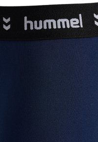 Mörkblå leggings med en strukturerad tyg och en svart elastisk midja som har vit "hummel" branding och chevronmönster.