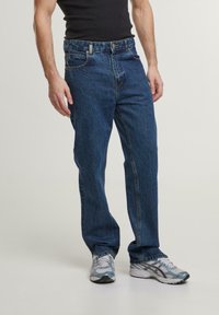 Jeans din denim de culoare albastră închisă, cu o croială dreaptă, cinci buzunare și o ușoară estompare. Potrivite cu adidași gri.