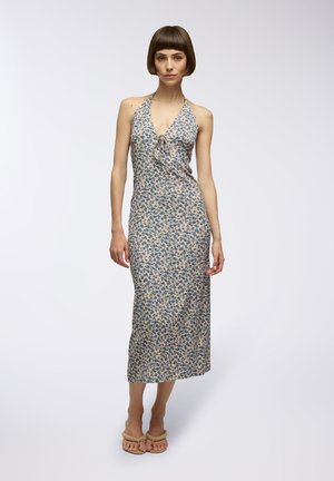 Abito a halter floreale in crema con motivi di fiori blu, corpino aderente e lunga gonna. La modella indossa sandali beige.