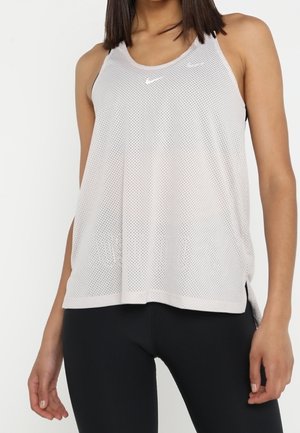 Vrouw draagt een loszittend, lichtgrijs, mesh Nike tanktopje en zwarte legging, staand tegen een witte achtergrond.