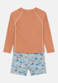 Rash guard in peach with long sleeves, paired with blue shorts featuring multi-colored dinosaur patterns. Smooth fabric, sporty design.