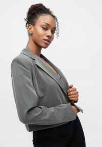 Sacou gri croitorit, cu guler structurat, închidere cu un singur nasture și mâneci lungi. Material neted, cu o textură subtilă.