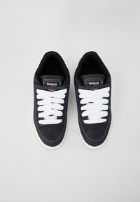Sneakers de camurça preta com atacadores brancos e solas de borracha, apresentando um colar almofadado, detalhes perfurados e um rótulo de logótipo na língua.