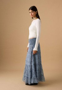 Top bianco a maniche lunghe con costine abbinato a una gonna lunga blu con motivo, vita arricciata e orlo a balze sovrapposte.