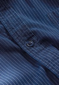 Cămașă bleumarin cu nasturi, cu dungi albe fine; prezintă un nasture întunecat cu patru găuri și un material moale, texturat.